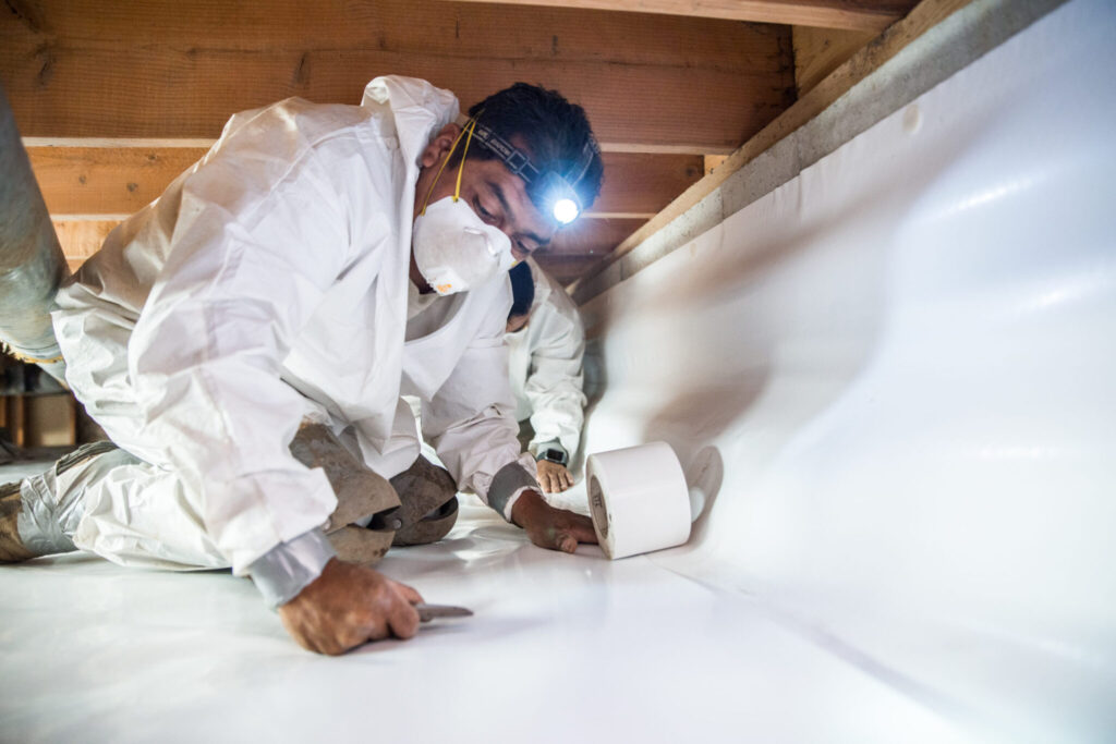 Crawl pros professionals laying down protective material for a crawl space encapsulation