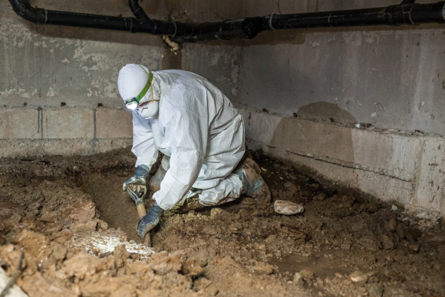 Crawl space company professional digs trenches in crawl space before sump pump installation