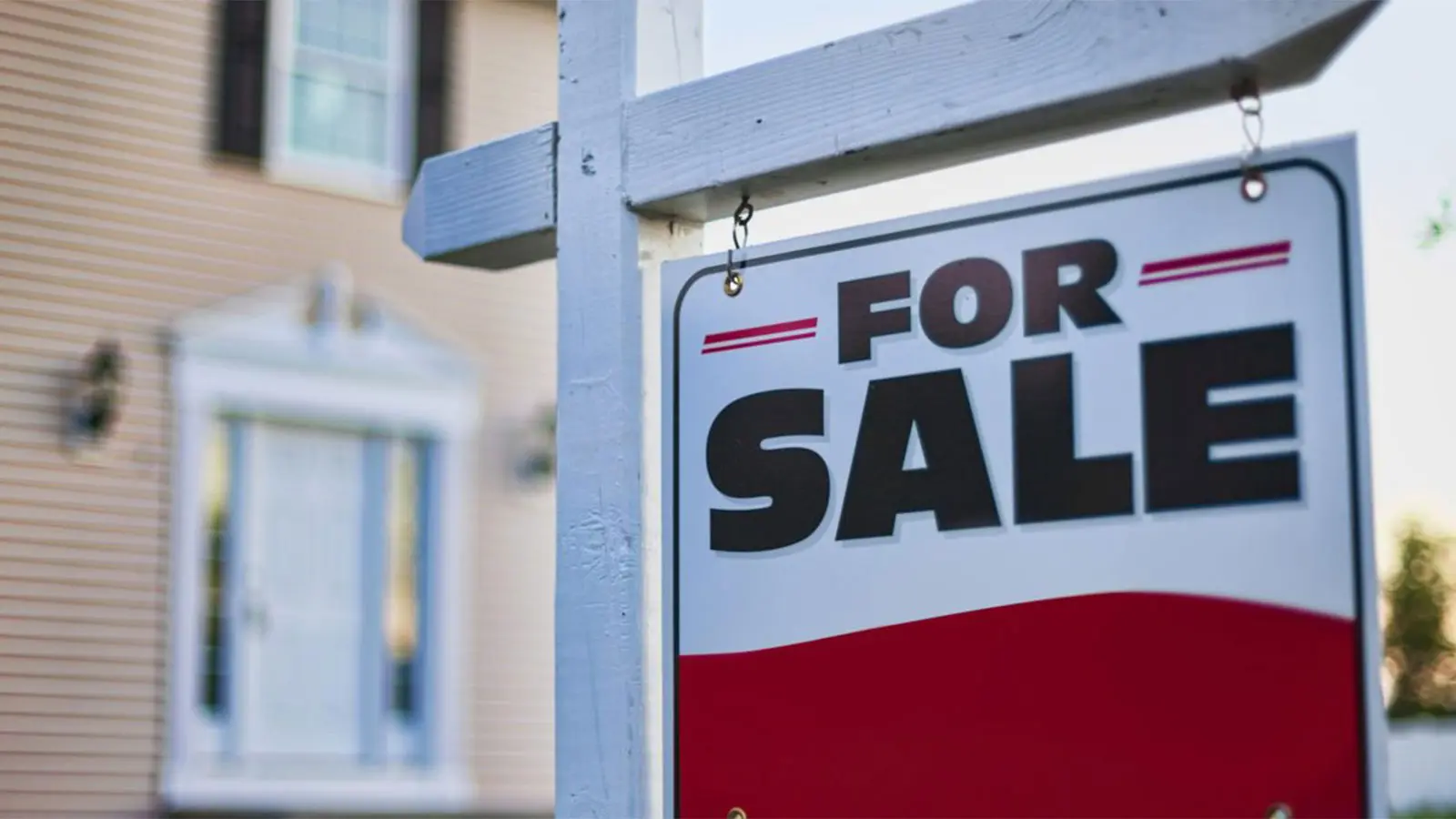 For sale sign hung on a white picket fence post outside of a home