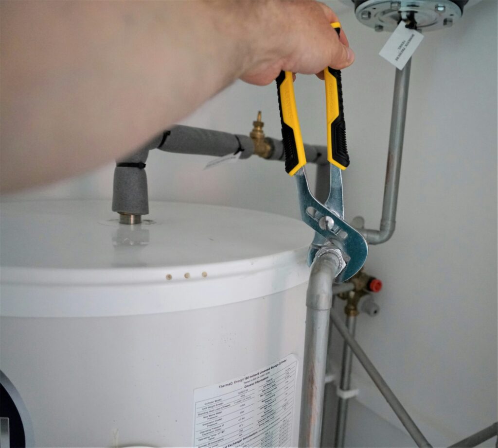 Plumber performing crawl space residential plumbing services by tightening a water pipe using a wrench